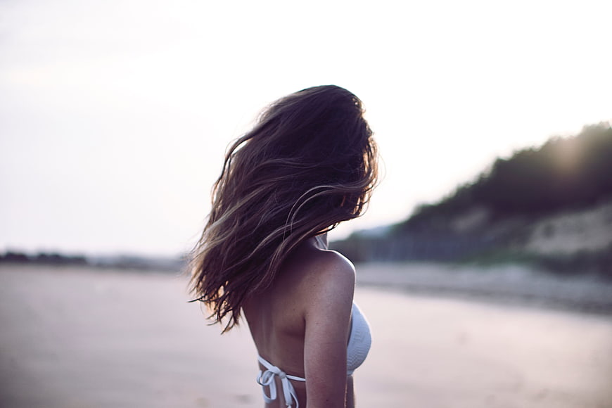 Woman in white bikini on beach with windblown hair at sunset