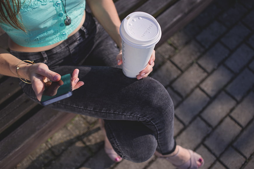 Woman on bench with coffee and smartphone