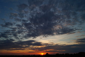 Dramatic sunset with textured clouds over dark silhouette landscape