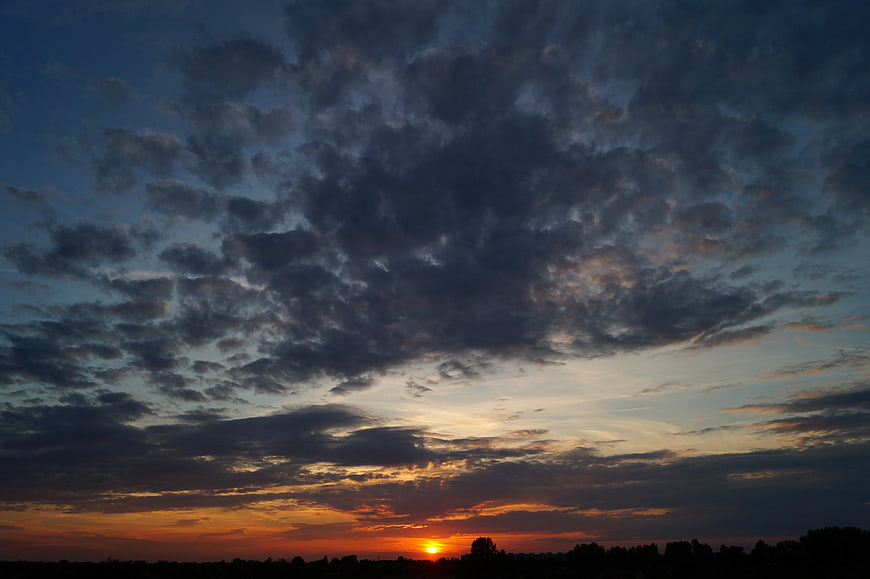 Dramatic sunset with textured clouds over dark silhouette landscape