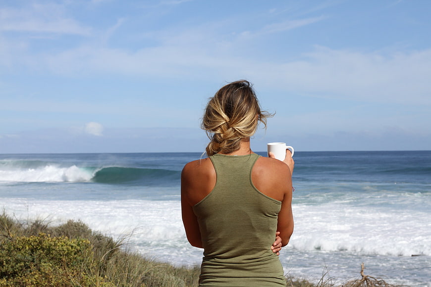 Woman drinking coffee while looking at ocean waves