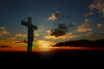 Silhouette of a wooden crucifix against a dramatic sunset sky