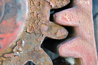 Close-up of rusted metal gear teeth with cracked red paint