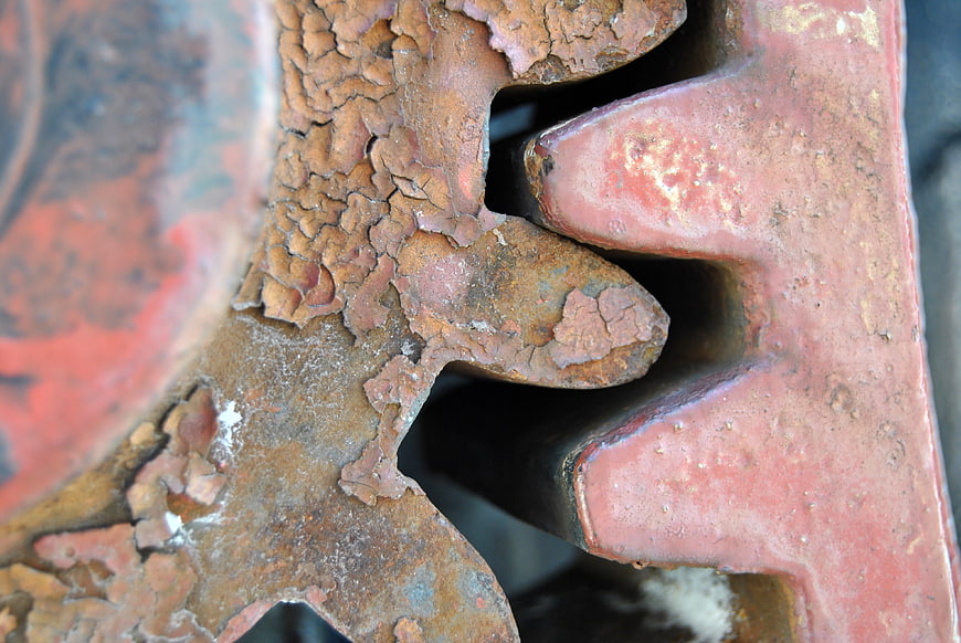 Close-up of rusted metal gear teeth with cracked red paint