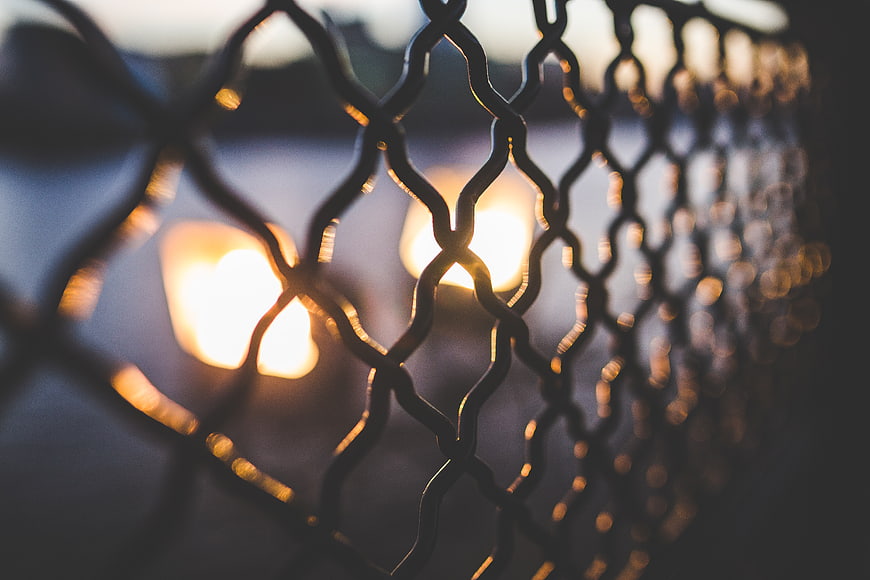 Close-up of chain-link fence with warm bokeh lights