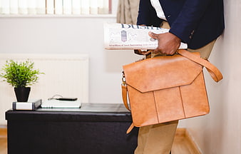 Businessman holding leather briefcase and newspaper in office