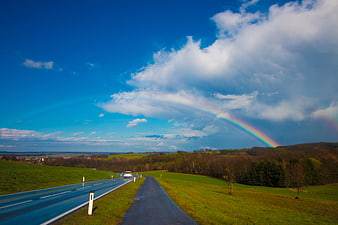 Rainbow over winding country road with car and green hills