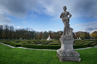 Classical statue in formal garden with manicured hedges