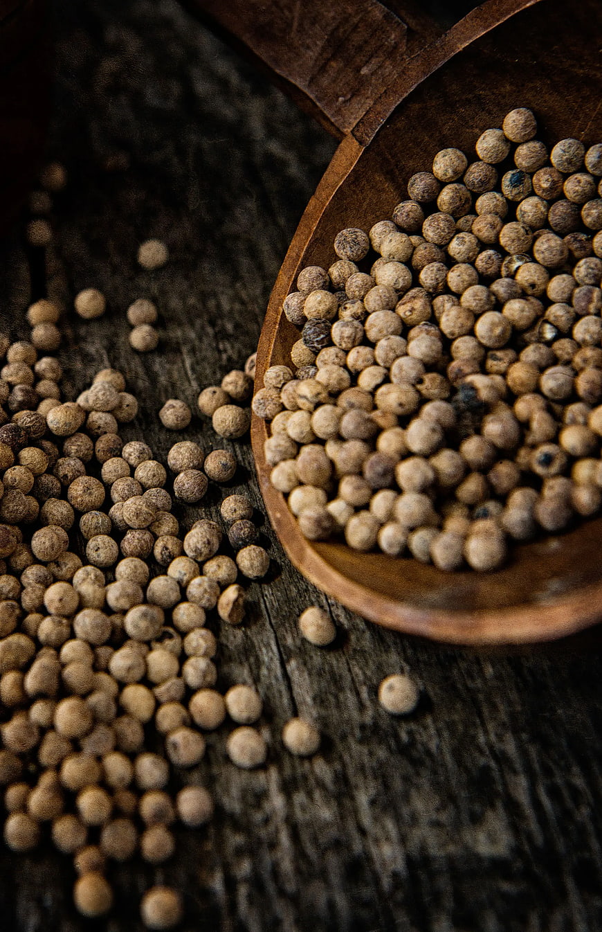 White peppercorns in wooden spoon on rustic table