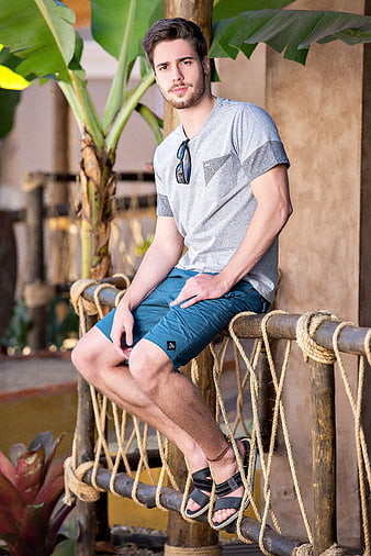 Young man in casual summer fashion sitting on rustic rope railing
