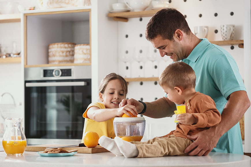 Happy father and children making fresh orange juice in kitchen