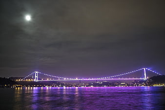 Istanbul Bosphorus Bridge illuminated in purple at night with moon