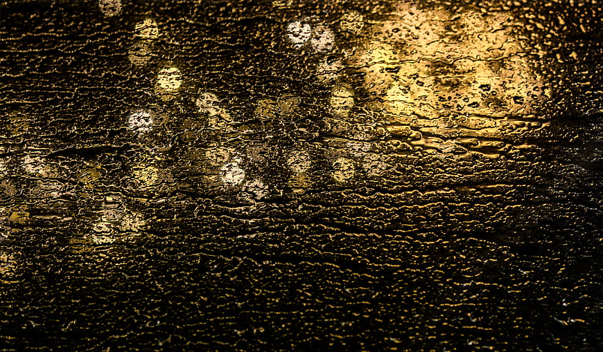 Golden raindrops on wet surface with bokeh lights