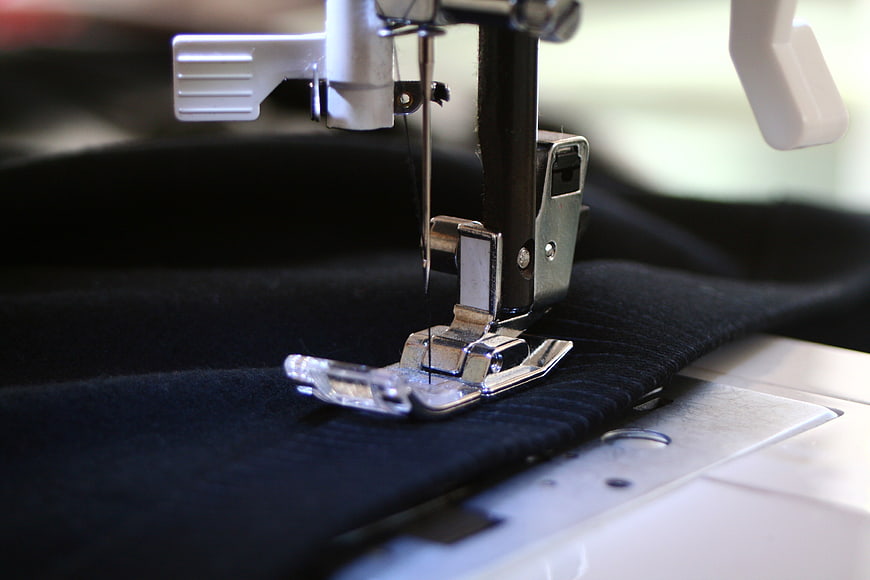 Close-up of sewing machine needle stitching black fabric
