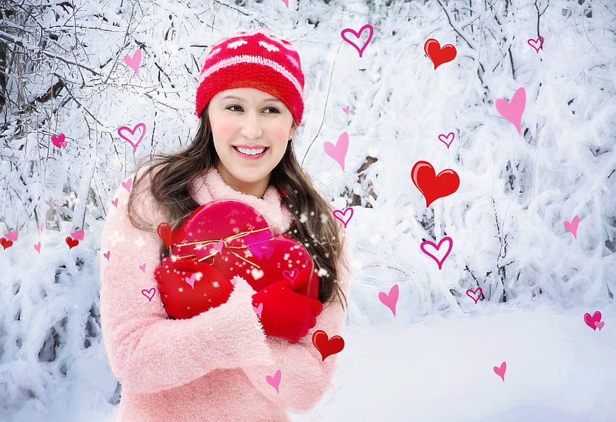 Happy woman holding heart gift in snowy winter forest