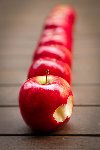 Line of red apples with bite taken out on wooden table