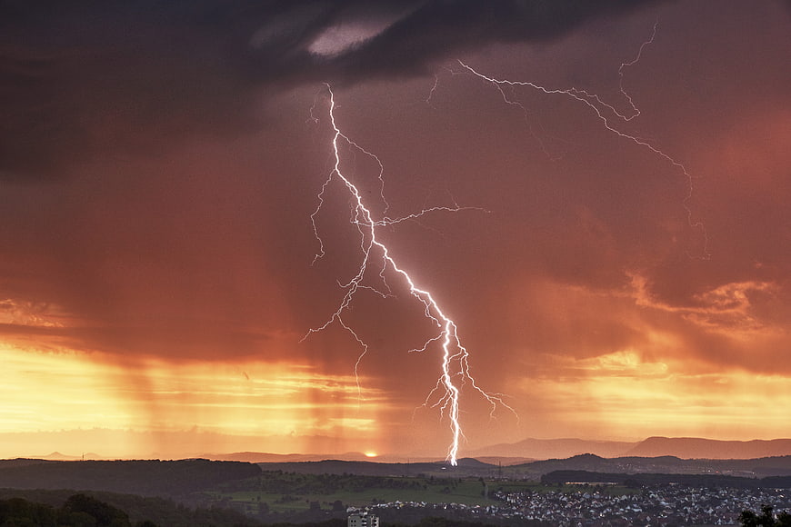 Dramatic Lightning Strike Over Rolling Hills at Sunset