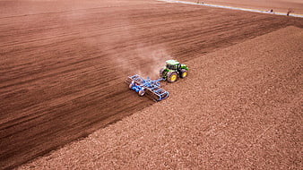 Aerial view of green tractor tilling vast brown agricultural field