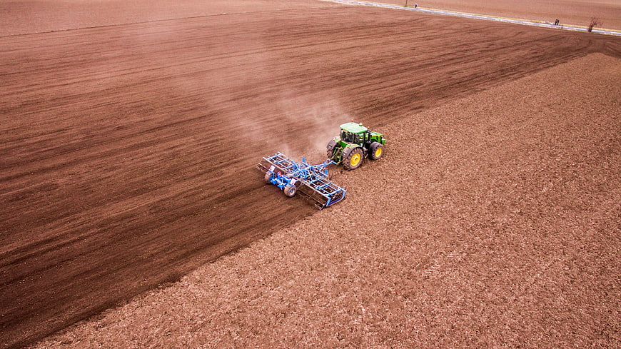 Aerial view of green tractor tilling vast brown agricultural field