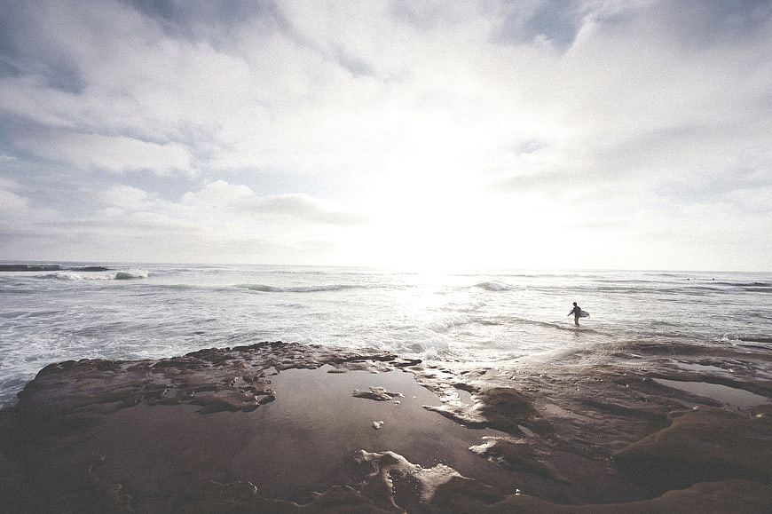 Surfer Walking on Rocky Beach at Sunset