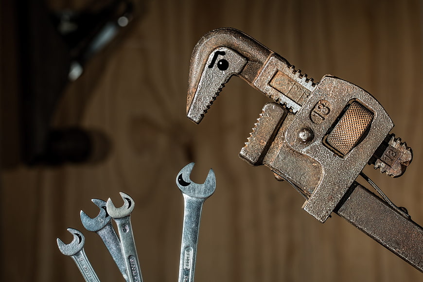 Rusty pipe wrench and spanners on wooden background