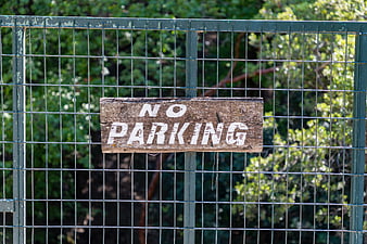 Weathered wooden no parking sign attached to a green metal wire fence