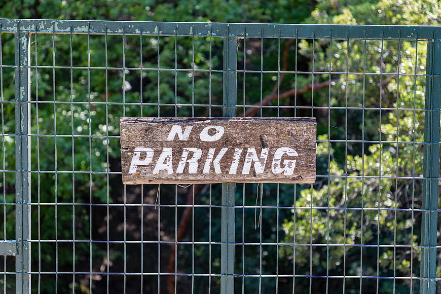 Weathered wooden no parking sign attached to a green metal wire fence