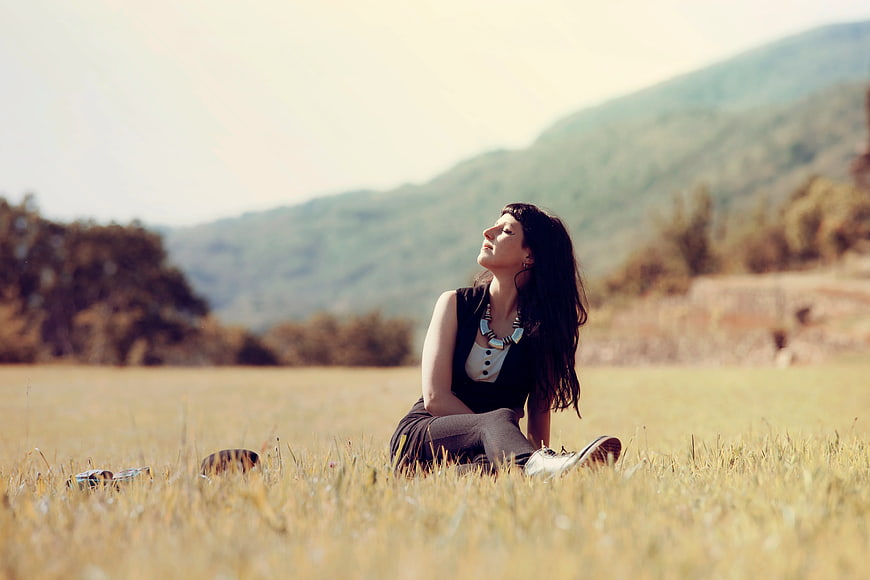Woman Sitting in Golden Field with Mountain Background