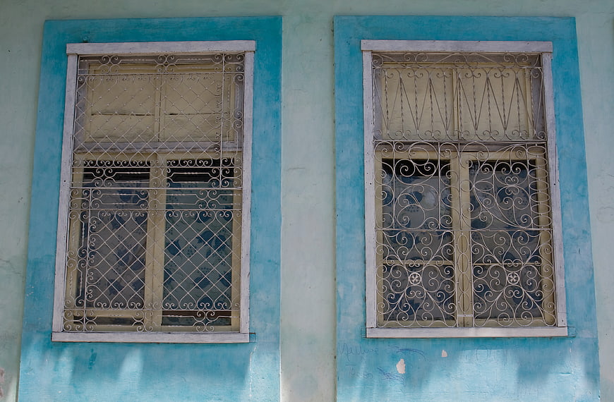 Two blue windows with ornate iron grilles on a weathered wall