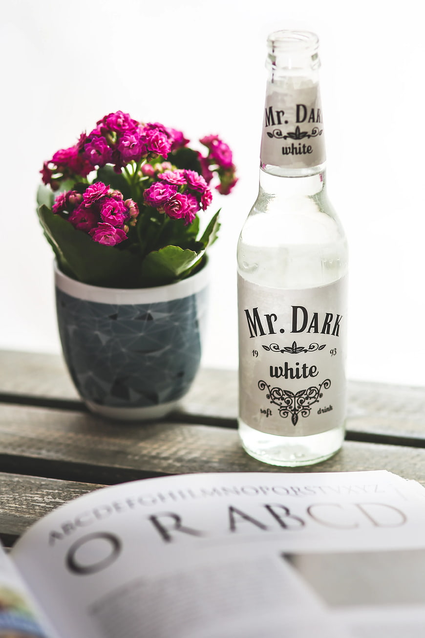Mr. Dark White Cola Bottle with Pink Flowers on Wooden Table