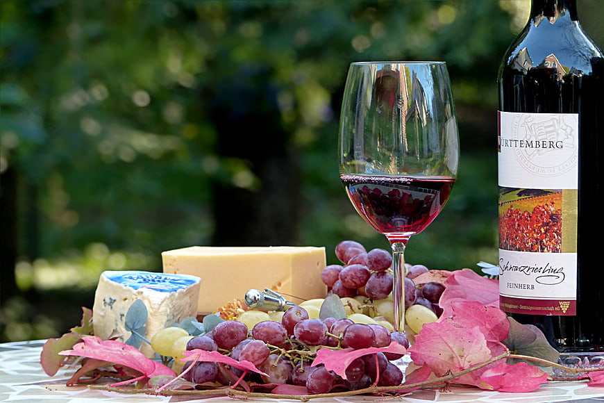 Red wine, cheese, and grapes on a table with autumn leaves