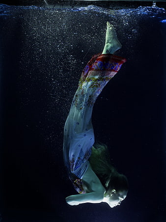 Woman in flowing dress diving underwater in dark water