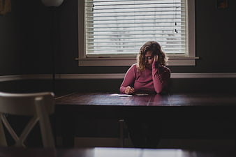 Sad woman writing at table in dim room