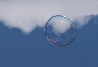 Iridescent Soap Bubble Floating Against Blue Sky And Clouds