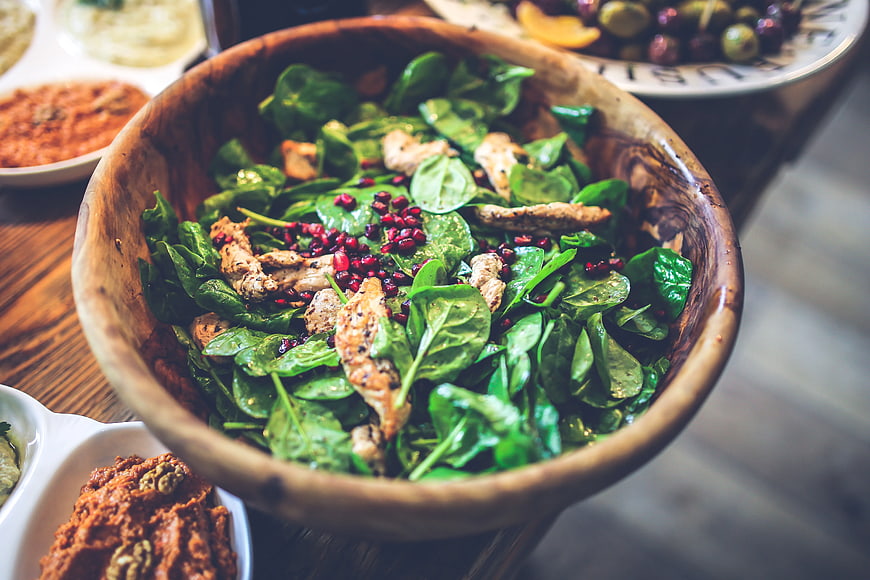 Fresh spinach chicken salad with pomegranate seeds in wooden bowl
