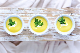 Top view of three bowls of yellow soup with parsley garnish