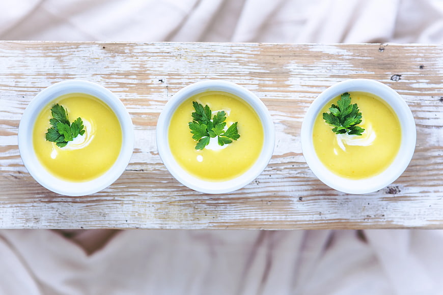 Top view of three bowls of yellow soup with parsley garnish