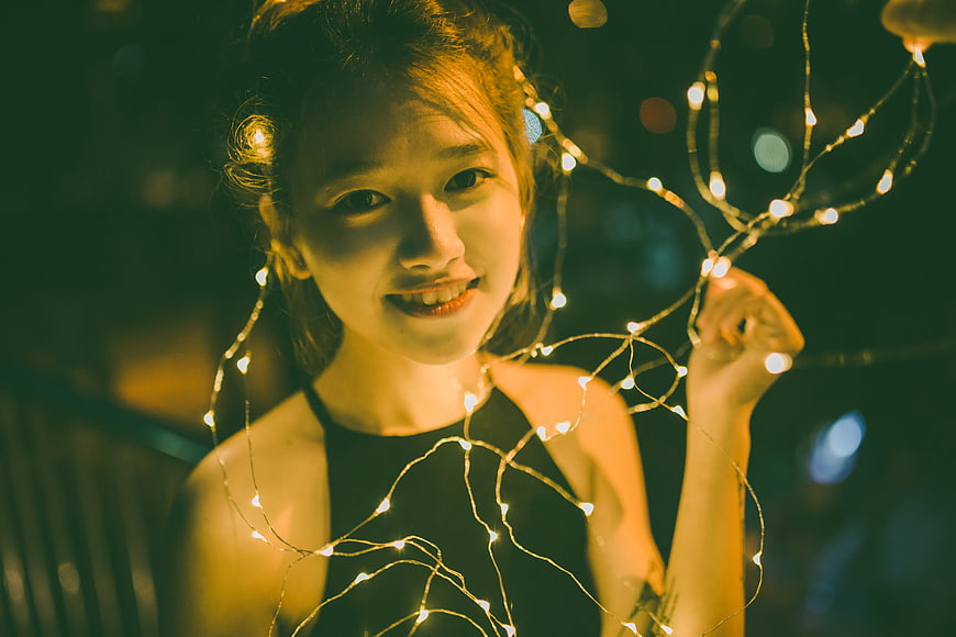Smiling Asian Woman Holding Fairy Lights at Night