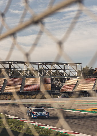 Race car speeding on track seen through safety fence