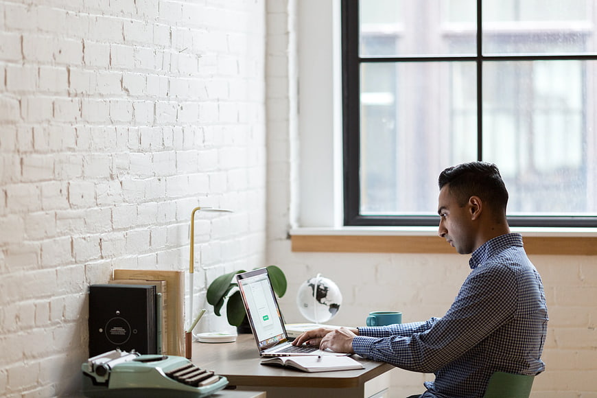 Man working on laptop in modern office with white brick wall