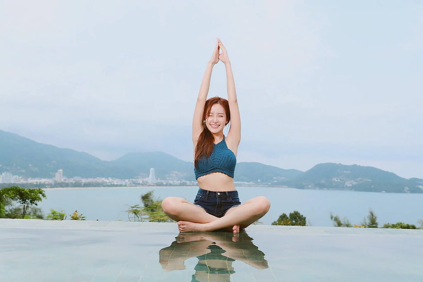 Woman doing yoga by infinity pool with ocean view