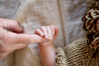 Close-up of newborn baby holding adult finger