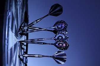 Close-up of darts hitting a dartboard with blue lighting