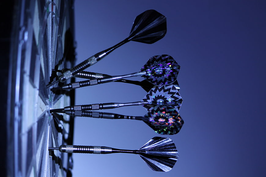 Close-up of darts hitting a dartboard with blue lighting