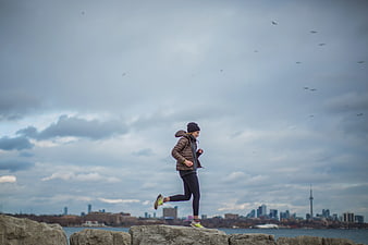 Woman Running on Rocks with City Skyline Background