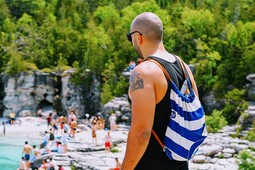 Man with Backpack Overlooking Crowded Natural Swimming Hole