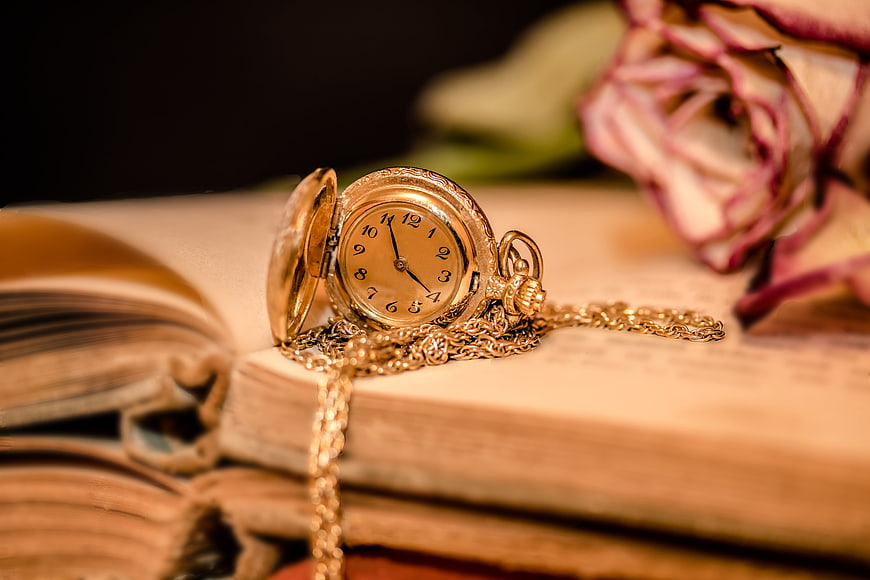 Vintage gold pocket watch on old book with dried rose