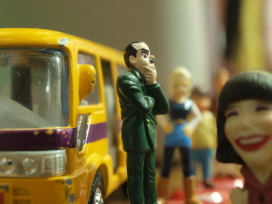Toy Man in Green Suit Standing by Yellow Bus