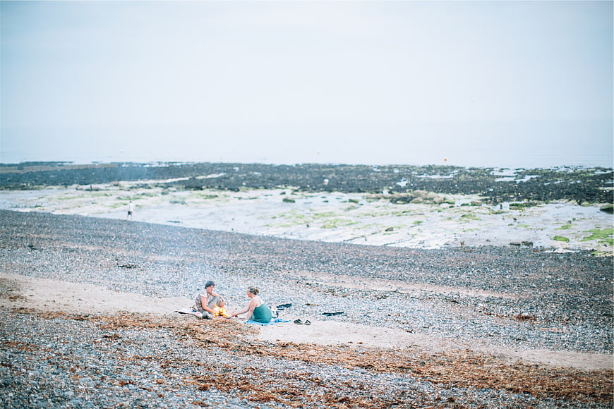Couple having a bonfire on a pebble beach at low tide
