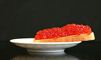 Slice of bread topped with red salmon caviar on a white plate